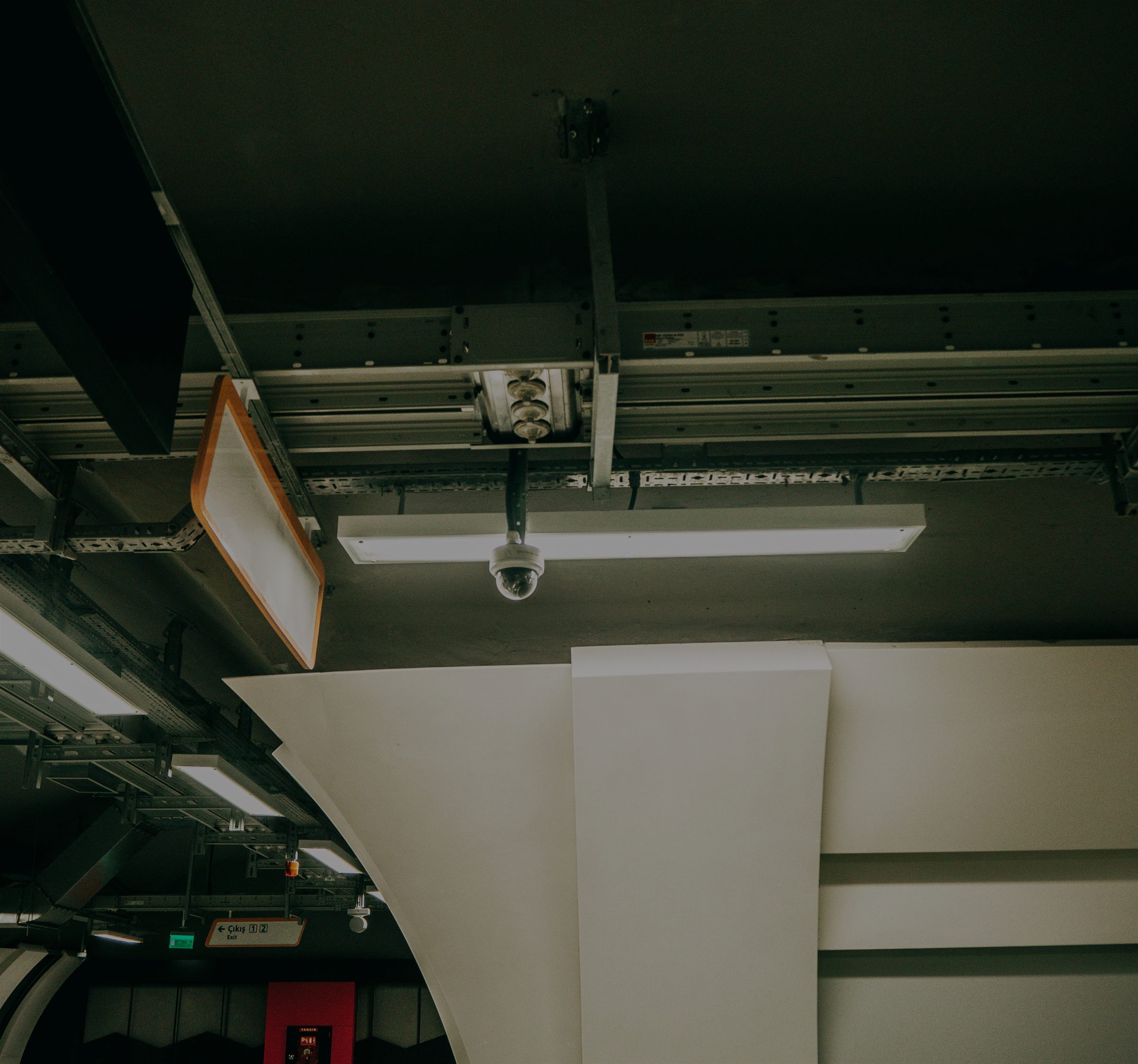Ceiling-mounted security camera and cable trays above a monitored facility corridor